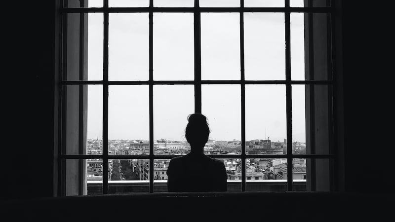 black-white-shot-lonely-female-standing-front-windows-looking-buildings