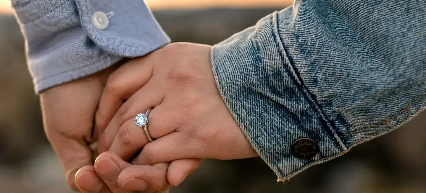 Two hands held together, one wearing a ring set with a diamond