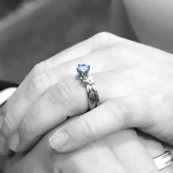 A hand wearing a ring with a blue memorial diamond