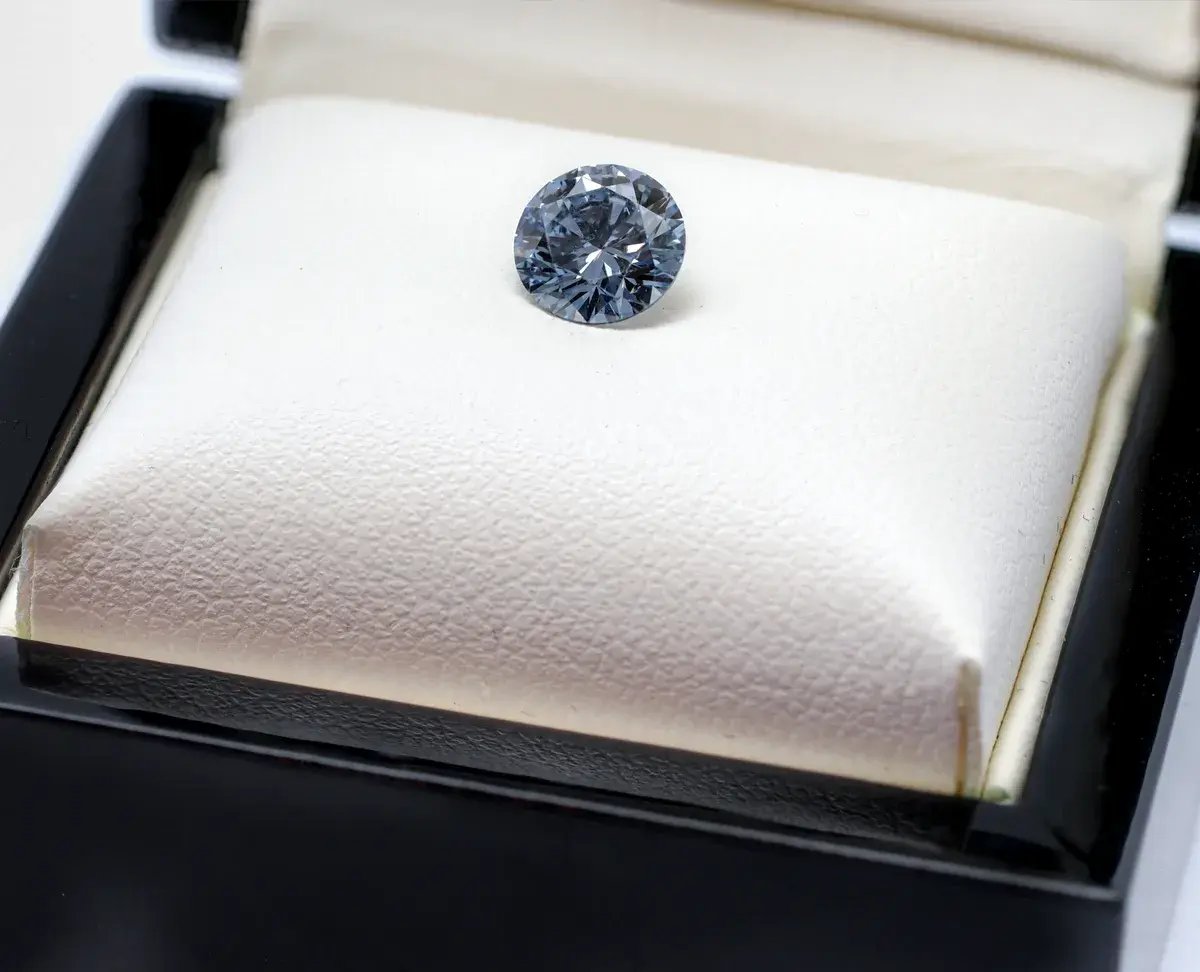 A blue memorial diamond resting on a cream leather cushion in an open black presentation box
